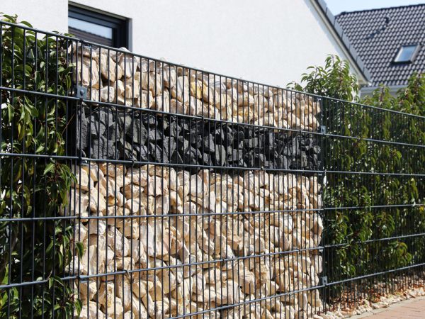 Végétaux et galets de différentes couleurs agrémentent ce mur de clôture utilisant des gabions